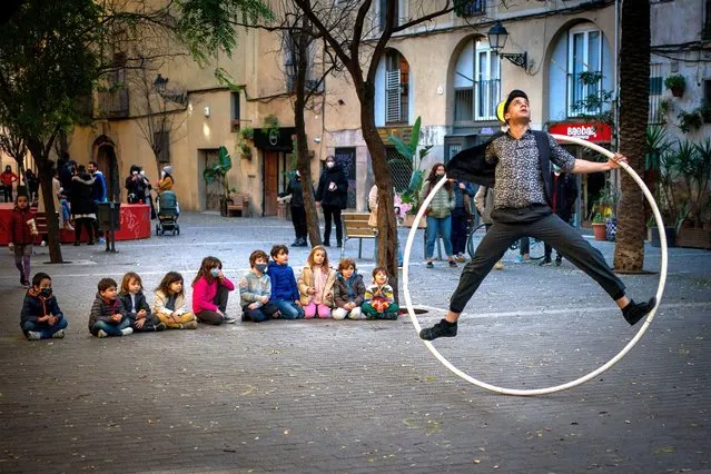 Children sit on the ground as they watch a street circus artist performing with a ring in Barcelona, Spain, Sunday, January 31, 2021. (Photo by Emilio Morenatti/AP Photo)