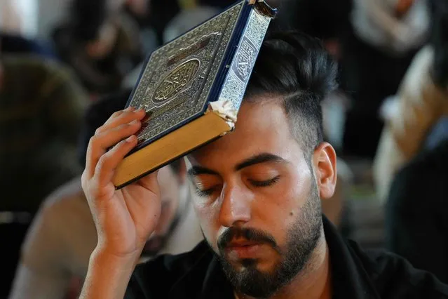 A Shiite Muslim worshipper places the Koran on his head during prayer rituals on “Laylat al-Qadr”, one of the holiest nights during the holy fasting month of Ramadan, at the Grand Mosque of Kufa, east of Iraq's central holy city of Najaf in the early hours of April 14, 2023. Laylat al-Qadr (Night of Destiny) marks the night Muslims believe the first verses of the Koran were revealed to Prophet Muhammad by the angel Gabriel in the seventh century. (Photo by Qassem Al-Kaabi/AFP Photo)