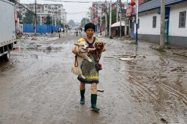 A resident holds two dogs as she walks in a village after remnants of Typhoon Doksuri brought rains and floods in Beijing, China on August 2, 2023. (Photo by Tingshu Wang/Reuters)