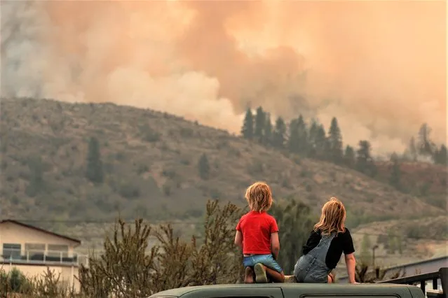 Locals gather to watch firefighting efforts amid heavy smoke from the Eagle Bluff wildfire, after it crossed the Canada-U.S. border from the state of Washington and prompted evacuation orders, in Osoyoos, British Columbia, Canada on July 30, 2023. (Photo by Jesse Winter/Reuters)