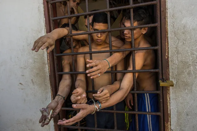 In this November 7, 2016 photo, suspects of violent crimes ask police for food, as one holds out money, from inside a holding cell at the municipal police station in Cumana, Sucre state, Venezuela. While police provide food, prisoners get most of their food and drinks from their families. (Photo by Rodrigo Abd/AP Photo)
