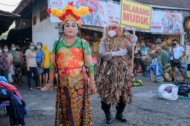 A police officer wears a Balinese traditional scary mask, locally known as Celuluk, as a traditional dancer educates people on the prevention of COVID-19 in Bali, Indonesia, 11 May 2021. Local police officers are using Balinese traditional characters to attract public attention in an attempt to provide education on COVID-19. (Photo by Made Nagi/EPA/EFE)