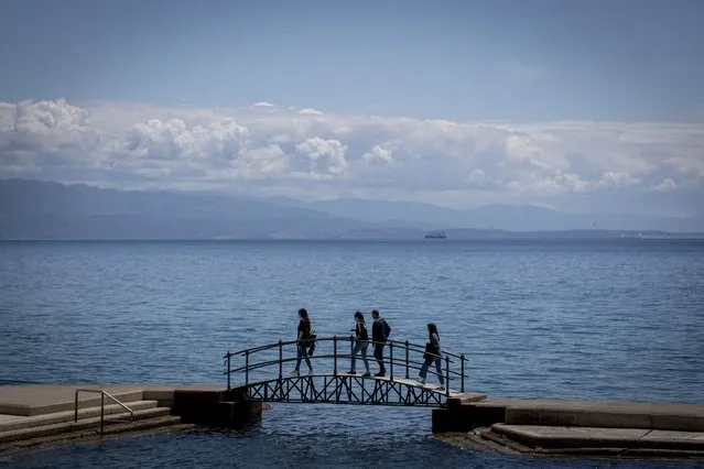 A group of tourists walk across a bridge on the seafront in Opatija, Croatia, Saturday, May 15, 2021. Croatia has opened its stunning Adriatic coastline for foreign tourists after a year of depressing coronavirus lockdowns and restrictions. (Photo by Darko Bandic/AP Photo)