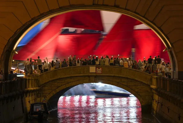 People watch a brig with scarlet sails floating on the Neva River during a rehearsal for the Scarlet Sails festivities marking school graduation in St. Petersburg, Russia, Thursday, June 24, 2021. (Photo by Dmitri Lovetsky/AP Photo)
