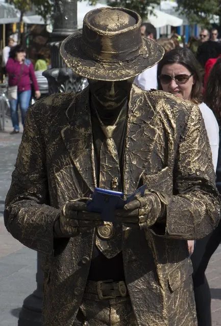 A human statue street artist takes a break to look at his cellphone in Madrid, Spain, Sunday, March 29, 2015. (Photo by Paul White/AP Photo)