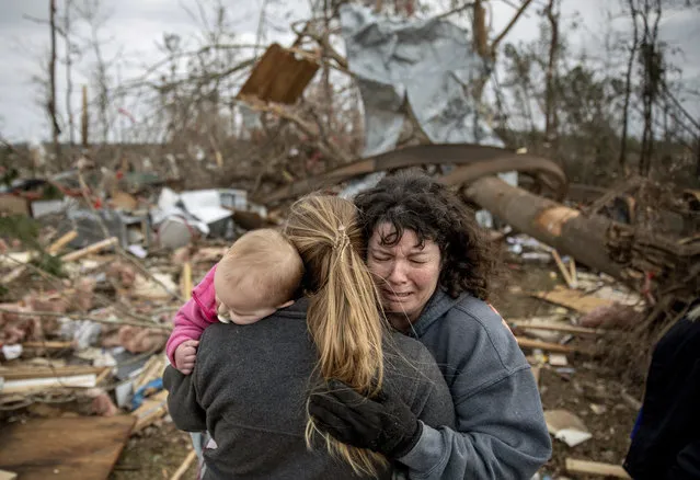 Carol Dean, right, cries while embraced by Megan Anderson and her 18-month-old daughter Madilyn, as Dean sifts through the debris of the home she shared with her husband, David Wayne Dean, who died when a tornado destroyed the house in Beauregard, Ala., Monday, March 4, 2019. “He was my wedding gift”, said Dean of her husband whom she married three years ago. “He was one in a million. He'd send me flowers to work just to let me know he loved me. He'd send me some of the biggest strawberries in the world. I'm not going to be the same”. (Photo by David Goldman/AP Photo)