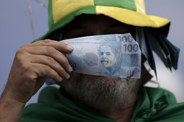 A demonstrator holds fake banknotes with an image of Brazil's former President Luiz Inacio Lula da Silva during a protest against Brazil's President Dilma Rousseff, part of nationwide protests calling for her impeachment, near the Brazilian national congress in Brasilia, Brazil, March 13, 2016. (Photo by Ueslei Marcelino/Reuters)