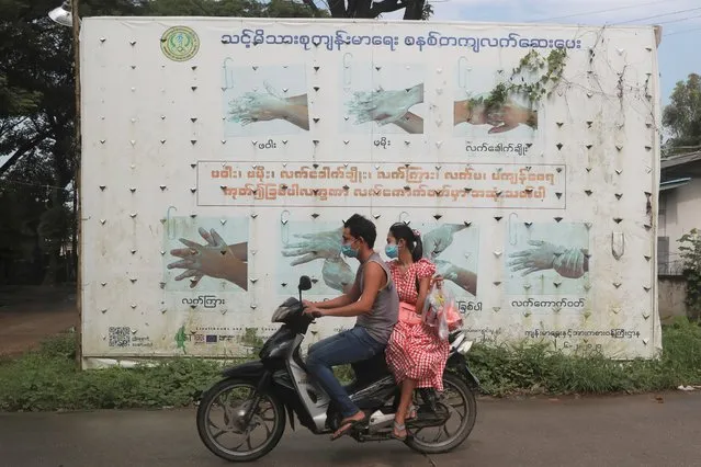 People wearing face masks ride a motorbike that drives past a Health Ministry public information campaign billboard about proper hand washing in Shwe Pyi Thar township in Yangon, Myanmar Wednesday, July 28, 2021. (Photo by Thein Zaw/AP Photo)