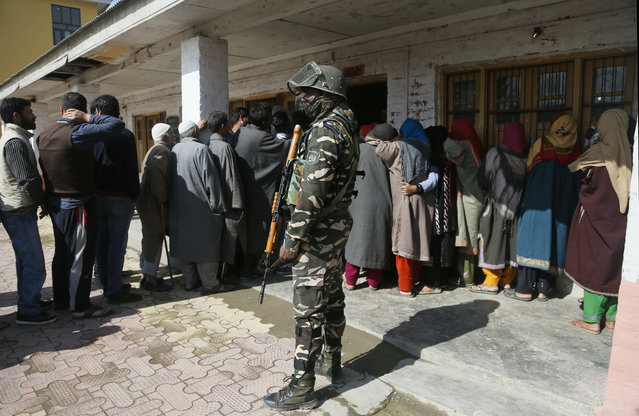 An Indian paramilitary soldier stands guard as Kashmiri voters wait in a queue to cast their votes outside a poling station during the second phase of India's general elections, on the outskirts of Srinagar, Indian controlled Kashmir, Thursday, April 18, 2019. Kashmiri separatist leaders who challenge India's sovereignty over the disputed region have called for a boycott of the vote. Most polling stations in Srinagar and Budgam areas of Kashmir looked deserted in the morning with more armed police, paramilitary soldiers and election staff present than voters. (Photo by Mukhtar Khan/AP Photo)