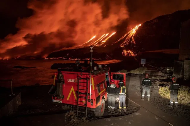 A handout photo made available by the Military Emergency Unit (UME) shows UME agents looking at the lava falling into the sea as Cumbre Vieja Volcano continues its activity in La Palma, Canary Islands, Spain, late 10 November 2021. Scientists continue to study if the increase of activity of the volcano is something occasional or it means the eruption is increasing once again after it had shown signs of decreasing activity. (Photo by Luismi Ortiz/Military Emergency Unit (UME)/EPA/EFE)