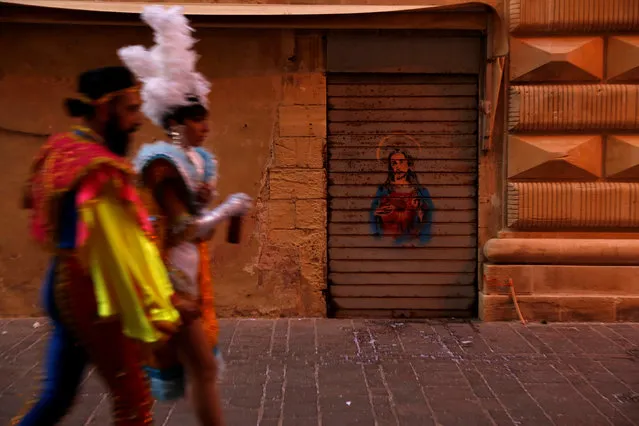 Costumed revellers walk past a shop shutter with graffiti depicting Jesus Christ on it during the carnival street parade in Valletta, Malta, February 25, 2017. (Photo by Darrin Zammit Lupi/Reuters)