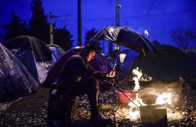 A refugee holds an umbrella as he tries to set a fire during rainy weather at a makeshift camp in the northern border village of Idomeni, Greece on April 8, 2016. A plan to send back migrants from Greece to Turkey sparked demonstrations by local residents in both countries days before the deal brokered by the European Union is set to be implemented. (Photo by Bulent Kilic/AFP Photo)