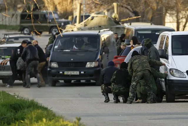 Members of pro-Russian self-defence units take cover behind cars outside a military base in the Crimean town of Belbek near Sevastopol March 22, 2014. (Photo by Vasily Fedosenko/Reuters)