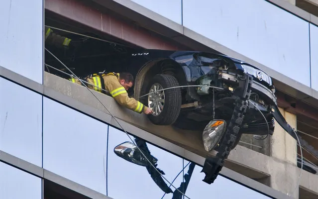 A firefighter secures a cable to the wheel of a car that went through the retaining wall on the seventh floor of the Damon West Parking Ramp in downtown Rochester, Minn. on Friday morning, March 28, 2014. The driver was uninjured and firefighters were eventually able to pull the car back through the retaining wall. (Photo by Jerry Olson/AP Photo/The Rochester Post-Bulletin)