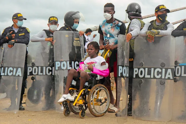 Police open the way to a woman on a wheelchair as a crowd of mix nationality migrants attempt to cross into Peru by the Friendship Bridge on the border with Brazil, 1,600 kilometers southeast of Lima, on February 16, 2021. Some 450 migrants, mostly Haitians, spent six days stranded on Wednesday trying unsuccessfully to enter Peru from Brazil via a border bridge in the Amazon, guarded by military and police, an AFP reporter observed. (Photo by Radio Madre de Dios/AFP Photo)
