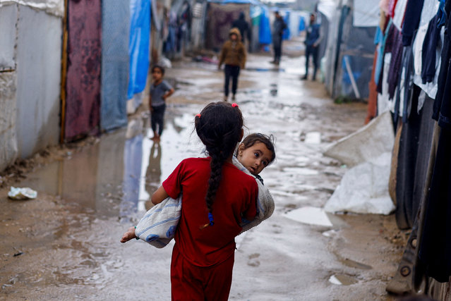 A displaced Palestinian girl holds a child as she walks at a tent camp on a rainy day, amid the ongoing conflict between Israel and Hamas, in Rafah, in the southern Gaza Strip on May 6, 2024. (Photo by Mohammed Salem/Reuters)