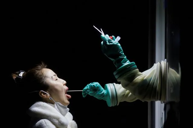 A woman receives a throat swab test at a street booth as the coronavirus disease (COVID-19) pandemic continues in Beijing, China, January 17, 2022. (Photo by Thomas Peter/Reuters)