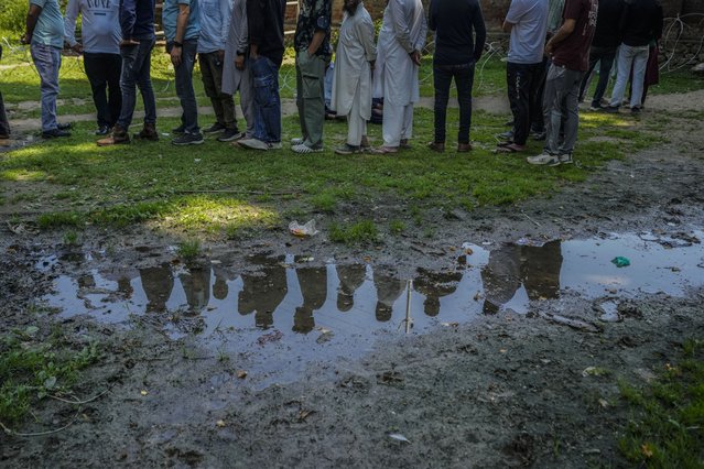 People standing in a queue to cast vote outside the polling booth are reflected in a puddle during the fifth round of multi-phase national elections in Sumbal north of Srinagar, Indian controlled Kashmir, Monday, May 20, 2024. (Photo by Mukhtar Khan/AP Photo)