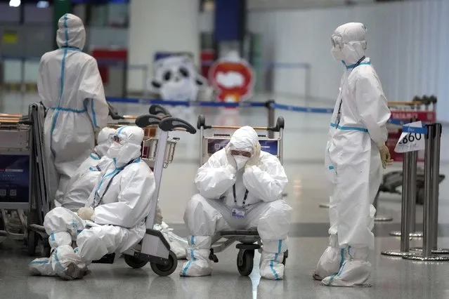 Olympic workers in protective clothing take a rest after helping travelers at the Beijing Capital International Airport after the 2022 Winter Olympics, Monday, February 21, 2022, in Beijing, China. (Photo by Frank Augstein/AP Photo)