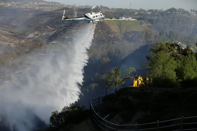 Firefighters look on as a helicopter drops water on a wildfire in the Rancho Santa Fe neighborhood Tuesday, May 13, 2014, in San Diego. Wildfires pushed by gusty winds chewed through canyons parched by California's drought, prompting evacuation orders for more than 20,000 homes on the outskirts of San Diego and another 1,200 homes and businesses in Santa Barbara County 250 miles to the north. (Photo by AP Photo)