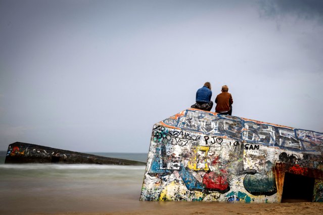 People look at the ocean sitting on the remain of a bunker from the Atlantic Wall, on May 19, 2024 near Cap Ferret, Southwestern France. The Atlantic Wall, ordered by Adolph Hitler and built between 1942 et 1944, was about 5000km long from Northern Norway to the French-Spanish border to defend occupied territories to be attacked by the sea side. 15 000 of them were planned to be built, but due to insufficient manpower and material, only about half of them were completed. (Photo by Olivier Morin/AFP Photo)