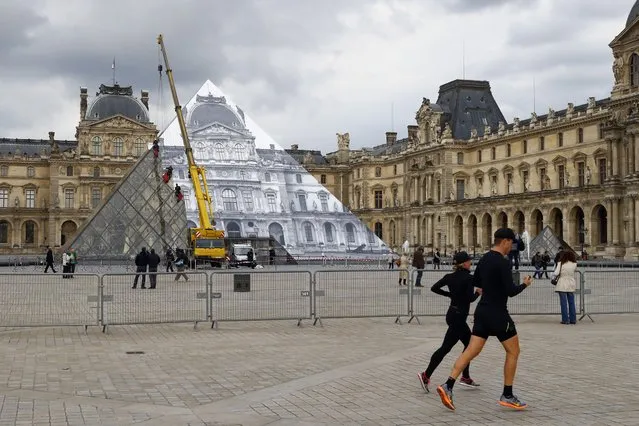 Joggers run as rope access technicians paste a giant picture on the Louvre Pyramid in background, as part of JR project in Paris, Monday, May 23, 2016. (Photo by Francois Mori/AP Photo)