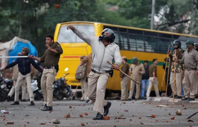 A police officer throws a stone towards protestors during a protest against the Citizenship Amendment Bill, a bill that seeks to give citizenship to religious minorities persecuted in neighbouring Muslim countries, outside the Jamia Millia Islamia University in New Delhi, India, December 13, 2019. (Photo by Adnan Abidi/Reuters)