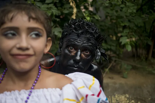 A man covered in motor oil, poses for a picture next to a girl dress a traditional clothes during a festivities in honor of Santo Domingo de Guzman in Managua, Nicaragua, Saturday, August 1, 2015. (Photo by Esteban Felix/AP Photo)