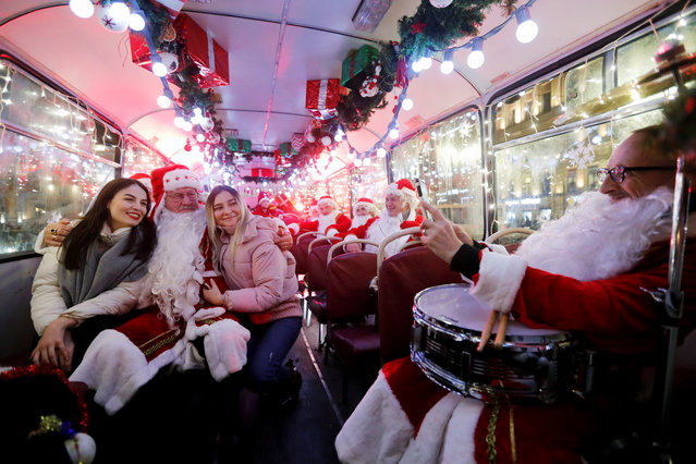 Musician dressed as Santa Claus takes a photo with passengers in a bus decorated for Christmas and New Year celebrations in central Saint-Petersburg, Russia on December 24, 2019. (Photo by Anton Vaganov/Reuters)