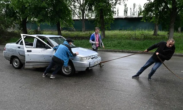 Local residents try to tow a damaged car in the Saltivka district, northern Kharkiv on May 29, 2022, amid Russian invasion of Ukraine. (Photo by Genya Savilov/AFP Photo)
