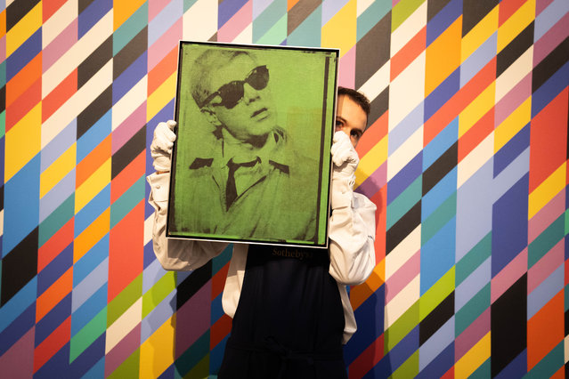 An art handler holds Andy Warhol's Self-Portrait on Friday, October 4, 2024 in front of Bridget Riley's Gaillard 2, during a preview for Sotheby's £200 million artwork sale, which includes works by Hockney, Warhol and Picasso. (Photo by James Manning/PA Images via Getty Images)