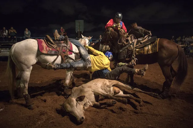 In this November 18, 2019 photo, cowboys compete to grab a bull's tail during a rodeo in Maracaibo, Venezuela. The sport is from Venezuela's cattle regions and is called “Coleo”, loosely meaning grabbing the tail. The downfall of Maracaibo has been especially brutal. Critics blame two decades of socialist rule for destroying the oil industry, that today produces a fraction of what it did at its height two decades ago. The Venezuelan government blames U.S. sanctions for many of its problems. (Photo by Rodrigo Abd/AP Photo)
