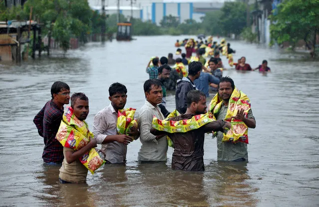 People carry packets of snacks after receiving them from civil defence volunteers in a flooded neighbourhood after heavy rains in Ahmedabad, July 27, 2017. (Photo by Amit Dave/Reuters)
