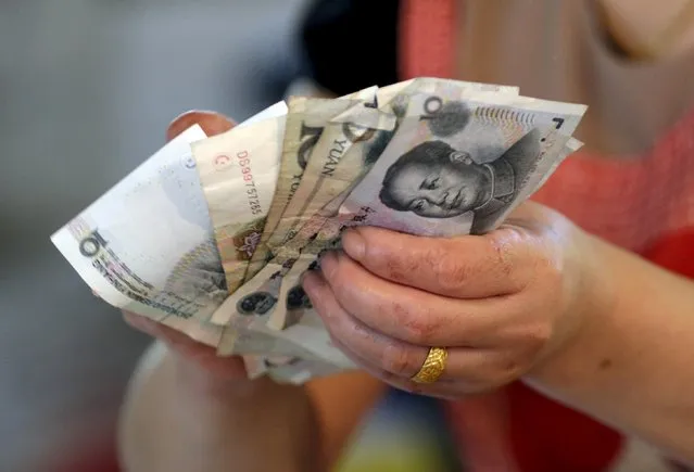 A vendor holds Chinese yuan notes at a market in Beijing in this August 12, 2015 file photo. China's yuan opened weaker against the dollar on August 17, 2015 but was stronger than the official midpoint fixed by the central bank. (Photo by Jason Lee/Reuters)