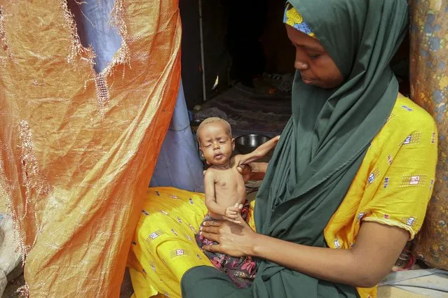 Amina Shuto, 21, who fled the drought-stricken Lower Shabelle area, holds her two-month old malnourished child at a makeshift camp for the displaced on the outskirts of Mogadishu, Somalia Thursday, June 30, 2022. The war in Ukraine has abruptly drawn millions of dollars away from longer-running humanitarian crises and Somalia is perhaps the most vulnerable as thousands die of hunger amid the driest drought in decades. (Photo by Farah Abdi Warsameh/AP Photo)