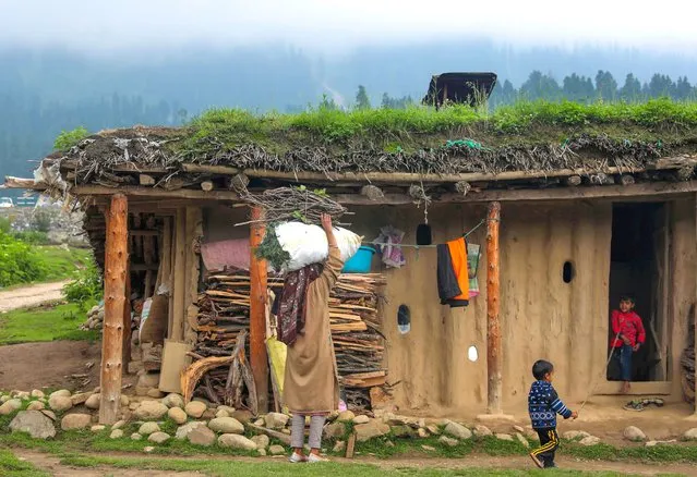 A gujjar nomadic member carry grass on her hand as she walks near mud houses in Doodhpathri, a tourist destination and hill station in district Budgam some 40 kilometers from Srinagar, the summer capital of Indian Kashmir, 17 July 2022 (issued 18 July 2022). The nomads live in the dhoks (mud houses) during their half-yearly stay in Kashmir and they leave these dhoks in winter when they move to warmer areas in Jammu region. The nomadic Gujjar and Bakerwal communities annually in summer start their migration towards the upper reaches of Kashmir in search of greener pastures for feeding their cattle. They move along with their baggage on horses and flocks of goats and sheep with ferocious dogs. (Photo by Farooq Khan/EPA/EFE)