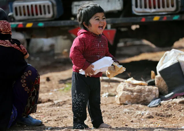 An Internally displaced Syrian child reacts as he holds bread at a makeshift camp in Azaz, Syria on February 20, 2020. (Photo by Khalil Ashawi/Reuters)