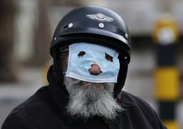 A man with a motorcycle helmet covers his face with a mask, as he watches municipal policemen order people to leave the corniche, or waterfront promenade, along the Mediterranean Sea, as the country's top security council and the government were meeting over the spread of coronavirus, in Beirut, Lebanon, Sunday, March 15, 2020. (Photo by Hussein Malla/AP Photo)