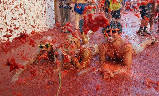 People lay in a puddle squashed tomatoes, during the annual “Tomatina” tomato fight fiesta in the village of Bunol, 50 kilometers outside Valencia, Spain, Wednesday, August 27, 2014. (Photo by Alberto Saiz/AP Photo)