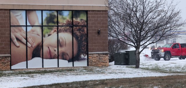A snow plow clears a restaurant's parking lot beside Massage Luxe in Kirkwood, Mo. as snow and sleet fall on Sunday, January 5, 2025. (Photo by Robert Cohen/St. Louis Post-Dispatch via AP Photo)