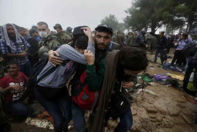 A Syrian refugee tries to protect his sisters as they walk through the mud to cross the border from Greece into Macedonia, near the Greek village of Idomeni, September 10, 2015. (Photo by Yannis Behrakis/Reuters)