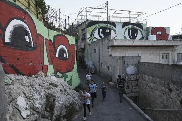 Palestinian children walk between murals that are part of the public art project “I Witness Silwan”,  in the Silwan neighbourhood of east Jerusalem, Friday, August 26, 2022. At right are the eyes of Silwan Community Member Nihad Siyam; at left, eyes inside two poppies, which Palestinians call their national flower. Eyes are always open in this flashpoint district. Now, new eyes emerged; they were painted on the walls of the decaying Palestinian homes. The eye murals, and graffiti of Palestinian symbols, are so giant that make you feel they are watching you wherever you walk in the neighborhood. (Photo by Mahmoud Illean/AP Photo)