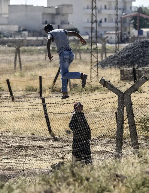 A Syrian looks on as a Kurdish man jumps over the border fence into the Syrian side during a demonstration near the Mursitpinar border crossing at Suruc in Sanliurfa province, on September 26, 2014. (Photo by Bulent Kilic/AFP Photo)