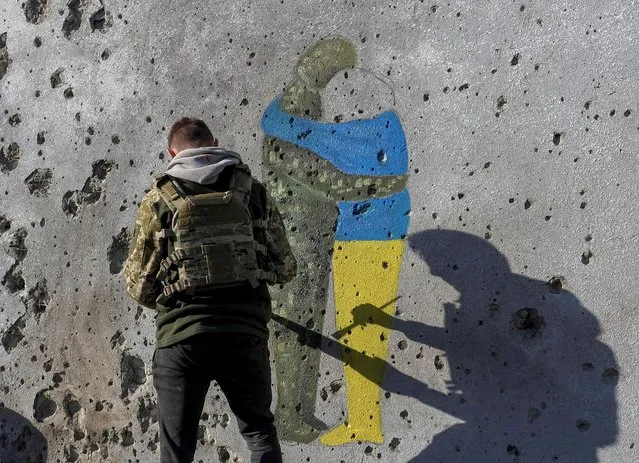 A Ukrainian artist paints a wall of a building covered with traces of bullets and shrapnel, amid Russia's attack on Ukraine, in Kupiansk, Ukraine on October 16, 2022. (Photo by Vyacheslav Madiyevskyy/Reuters)