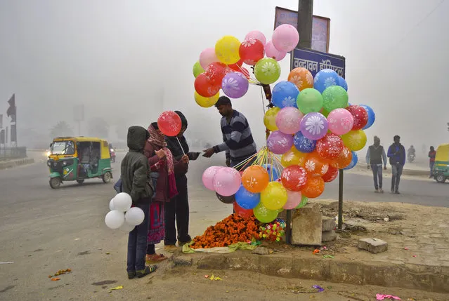 A man sells balloons and marigold flower garlands at a traffic roundabout on New Year's day in Greater Noida, outskirts of New Delhi, India, Monday, January 1, 2018. A lot of commuters were Monday buying balloons and flower garlands to decorate their vehicles, shops and houses on the first day of the New Year. Signage of a hospital in Hindi language is seen behind the balloons. (Photo by R.S. Iyer/AP Photo)
