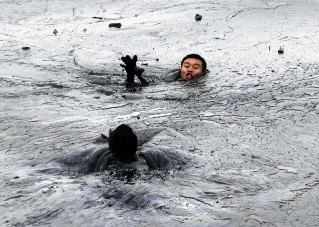 A firefighter rushes to aid his colleague who ran into trouble amid thick oil cover as they attempted to fix an underwater pump in Dalian, China. (Photo by Jiang He/Greenpeace/Associated Press)