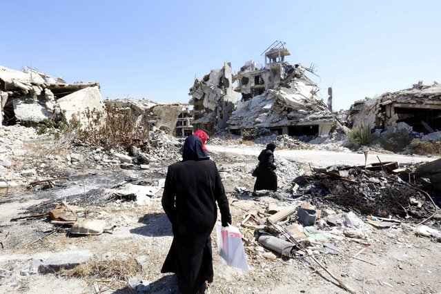 People walk between rubble in the city of Homs, Syria, 19 September 2016. According to media reports, the evacuation process of some 300 gunmen from the besieged neighborhood of al-Waer in Homs that was scheduled to be carried out on the same day has been postponed to the next day. The gunmen would head to the northwestern city of Idlib in accordance with a settlement agreement that was worked out between the Syrian government and the reconciliation committees in the area a year ago. A UN-backed three-phases agreement initiated in 2015 saw the evacuation of hundreds of residents from the neighborhood, whereby detainees held in government prisons would be released and the siege imposed on the area would be lifted. Al-Waer has been the only neighborhood under rebel control in Homs after government troops consolidated their grip over the city in 2014. An estimated 75 thousand people still live in al-Waer, down from about 300 thousand before the start of the Syrian conflict in 2011. (Photo by Youssef Badawi/EPA)