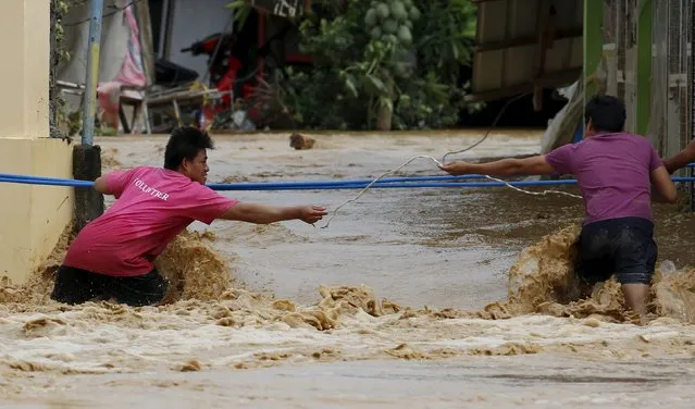 Residents use a plastic pipe and an electric wire to cross a flooded road amidst a strong current in Sta Rosa, Nueva Ecija in northern Philippines October 19, 2015, after it was hit by Typhoon Koppu. (Photo by Erik De Castro/Reuters)