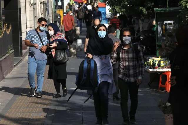 People wearing protective face masks to help prevent the spread of the coronavirus walk on a sidewalk in downtown Tehran, Iran, Sunday, September 20, 2020. Iran's president dismissed U.S. efforts to restore all U.N. sanctions on the country as mounting economic pressure from Washington pushed the local currency down to its lowest level ever on Sunday. (Photo by Vahid Salemi/AP Photo)