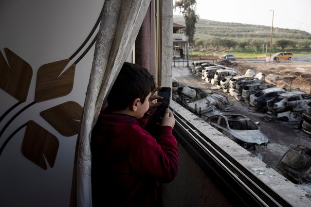A Palestinian boy stands in the ruins of his family apartment as he films vehicles torched in a rampage by settlers in Hawara, near the West Bank city of Nablus, Tuesday, February 28, 2023. On Sunday, two Israelis were killed by a Palestinian gunman in the northern West Bank, triggering a rampage in which Israeli settlers torched dozens of cars and homes in the Palestinian town and one Palestinian was killed. It was the worst such violence in decades. (Photo by Maya Alleruzzo/AP Photo)